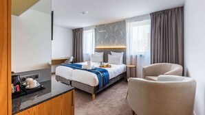 A hotel room with a bed, a chair, a desk with a coffee maker, and a window with curtains. - Brit Hotel Privilège Paris - Rosny (Rosny-sous-Bois)