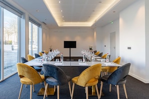 A conference room with a long table, chairs, a flat-screen TV, and a view of the outside. - Brit Hotel Privilège Paris - Rosny (Rosny-sous-Bois)