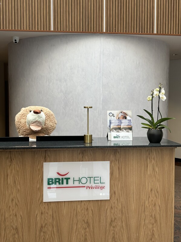 A reception desk with a plush toy, a potted orchid, and a sign for Brit Hotel. - Brit Hotel Privilège Paris - Rosny (Rosny-sous-Bois)