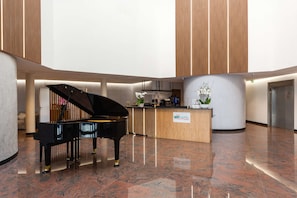 A grand piano in a spacious lobby with a reception desk and a sign for BRIT HOTEL. - Brit Hotel Privilège Paris - Rosny (Rosny-sous-Bois)