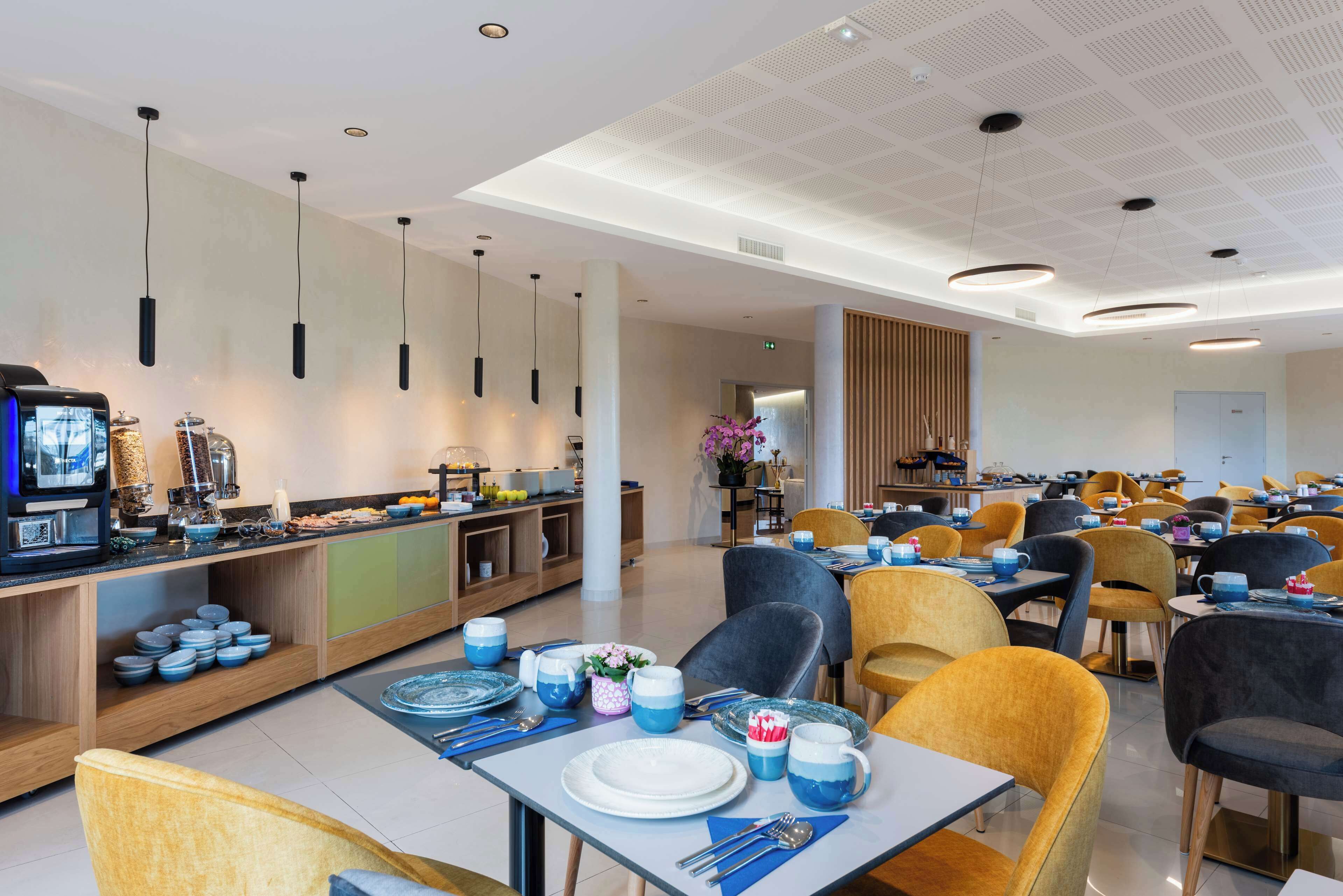 Un moderno comedor con varias mesas y sillas, un mostrador tipo buffet y lámparas colgantes.