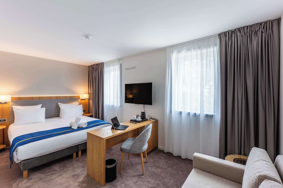 A hotel room with a bed, a desk, a chair, a TV, and a sofa.