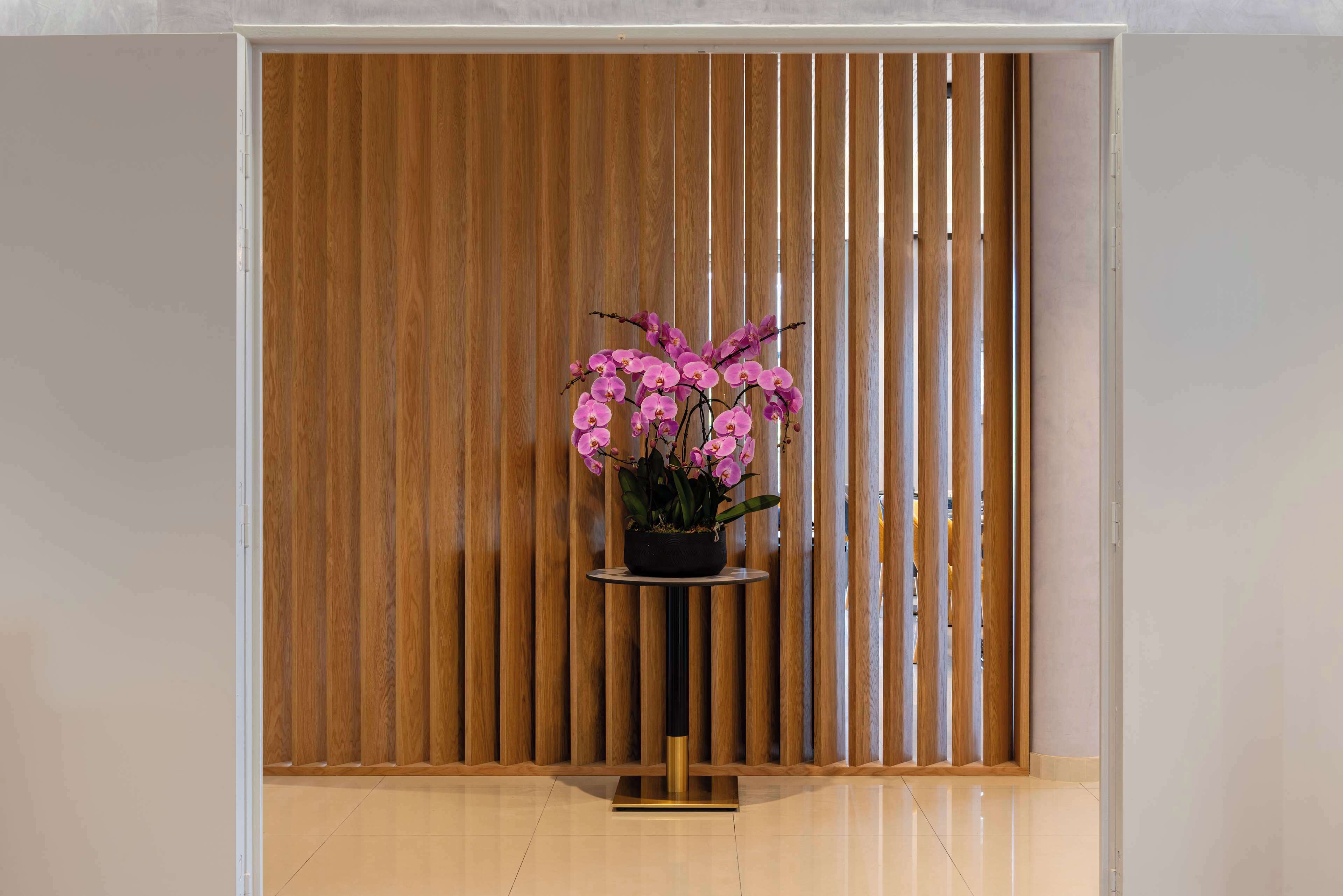 A room with a wooden slat partition, a small round table with a potted orchid, and a clean, tiled floor.
