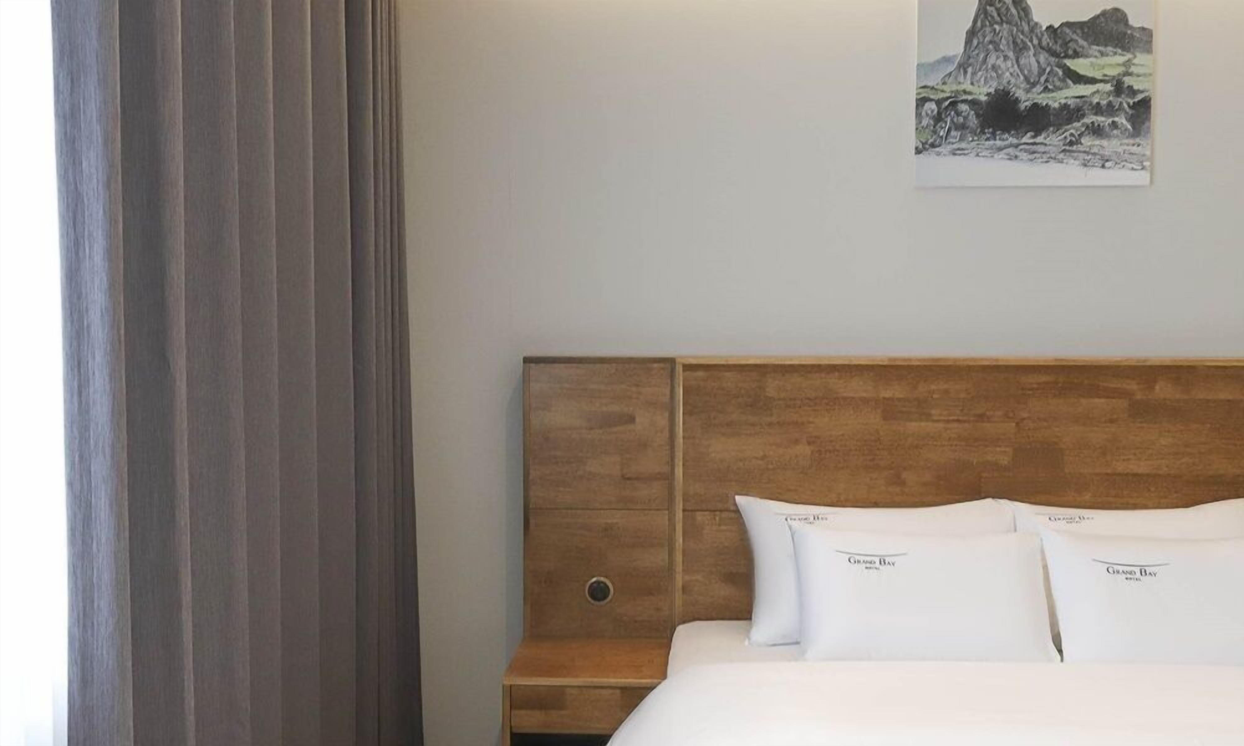 A hotel room with a wooden headboard, white bedding, and a painting of a mountainous landscape on the wall.