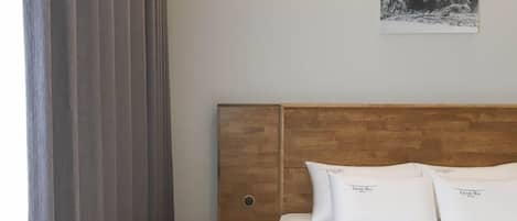 A hotel room with a wooden headboard, white bedding, and a painting of a mountainous landscape on the wall.