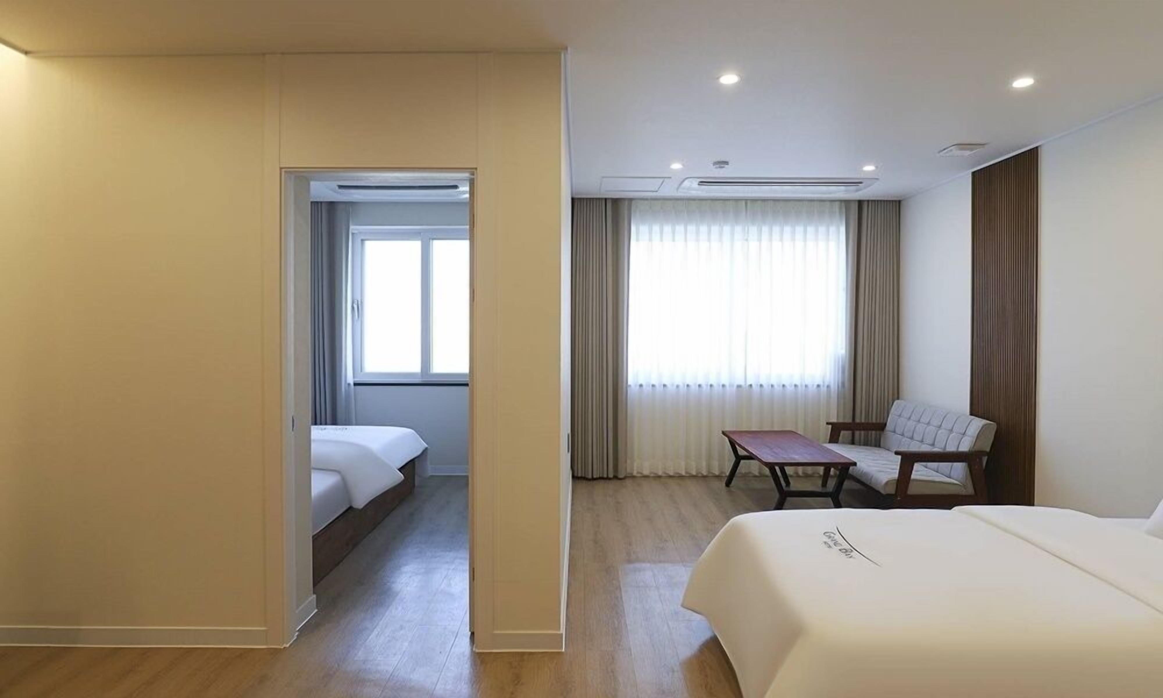 A hotel room with a bed, a desk, and a chair. There is a window with curtains and a door leading to another room.