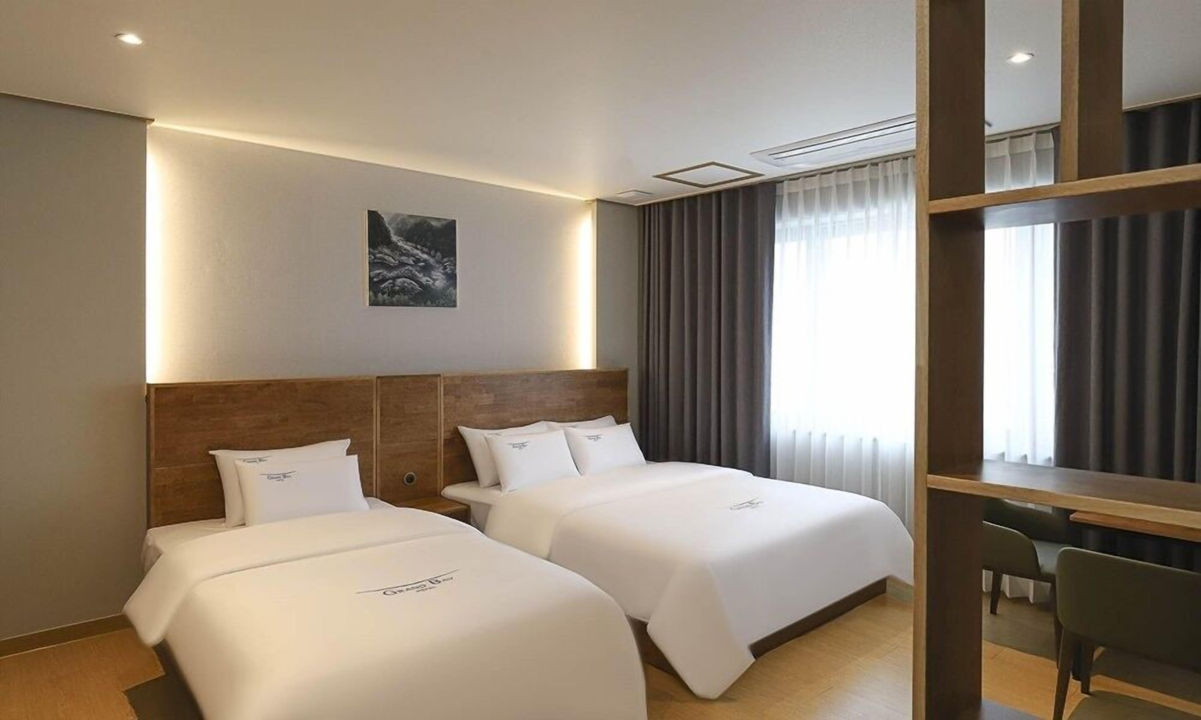 A hotel room with two beds, a desk, and a large window with curtains.