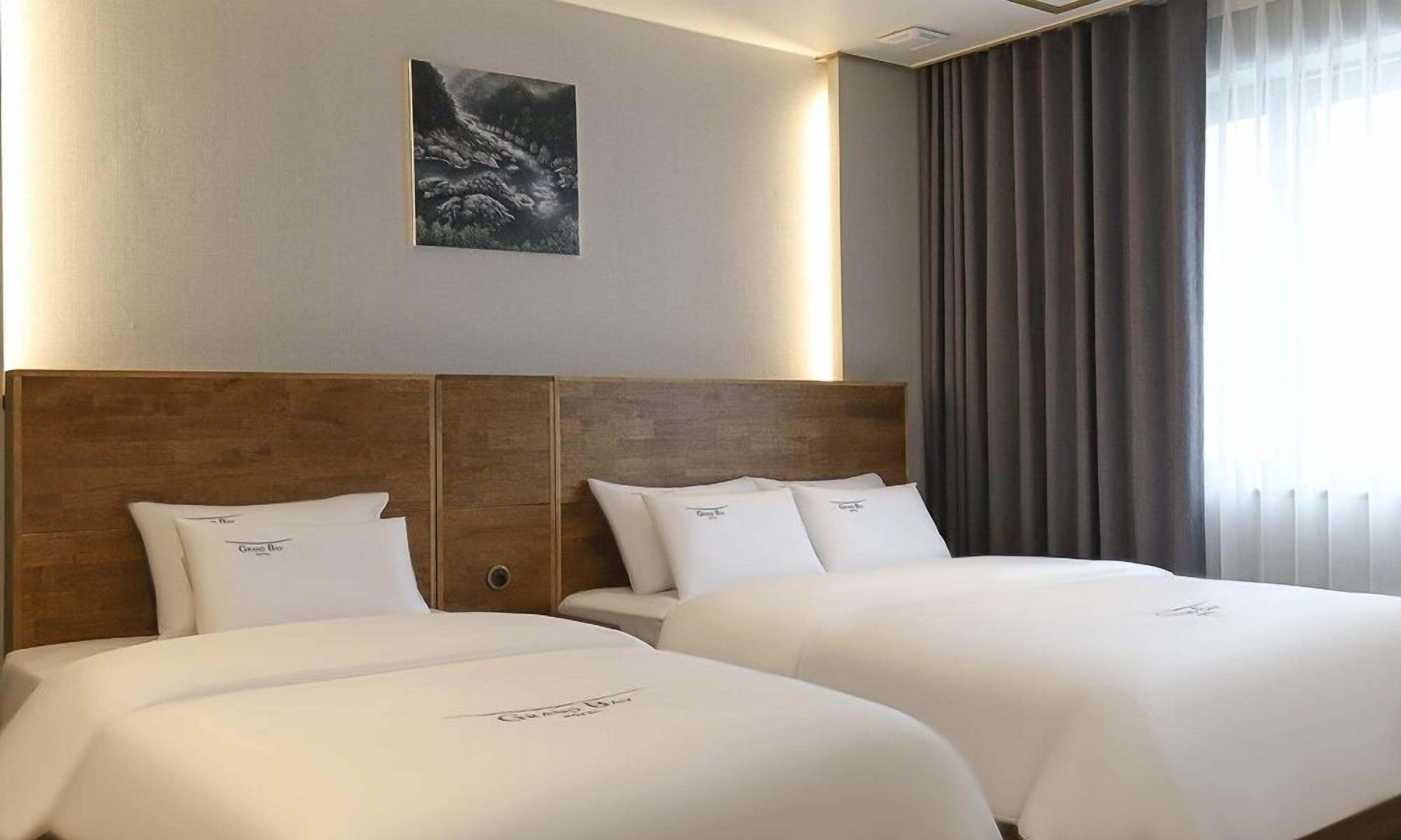 Een hotelkamer met twee bedden, een houten hoofdbord, een schilderij aan de muur en een raam met gordijnen.