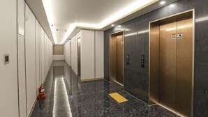 A hallway with a marble floor, a fire extinguisher, and two elevators. - Hotel Grand Bay Boryeong (Boryeong)