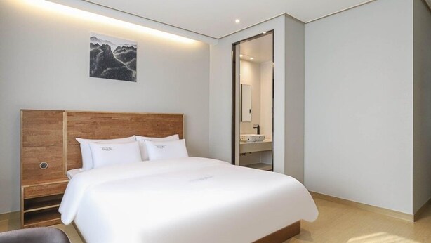 A modern hotel room with a large bed, wooden headboard, and a painting on the wall. - Hotel Grand Bay Boryeong (Boryeong)