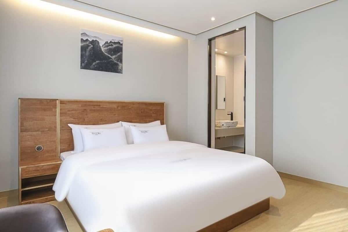 A modern hotel room with a large bed, wooden headboard, and a painting on the wall.