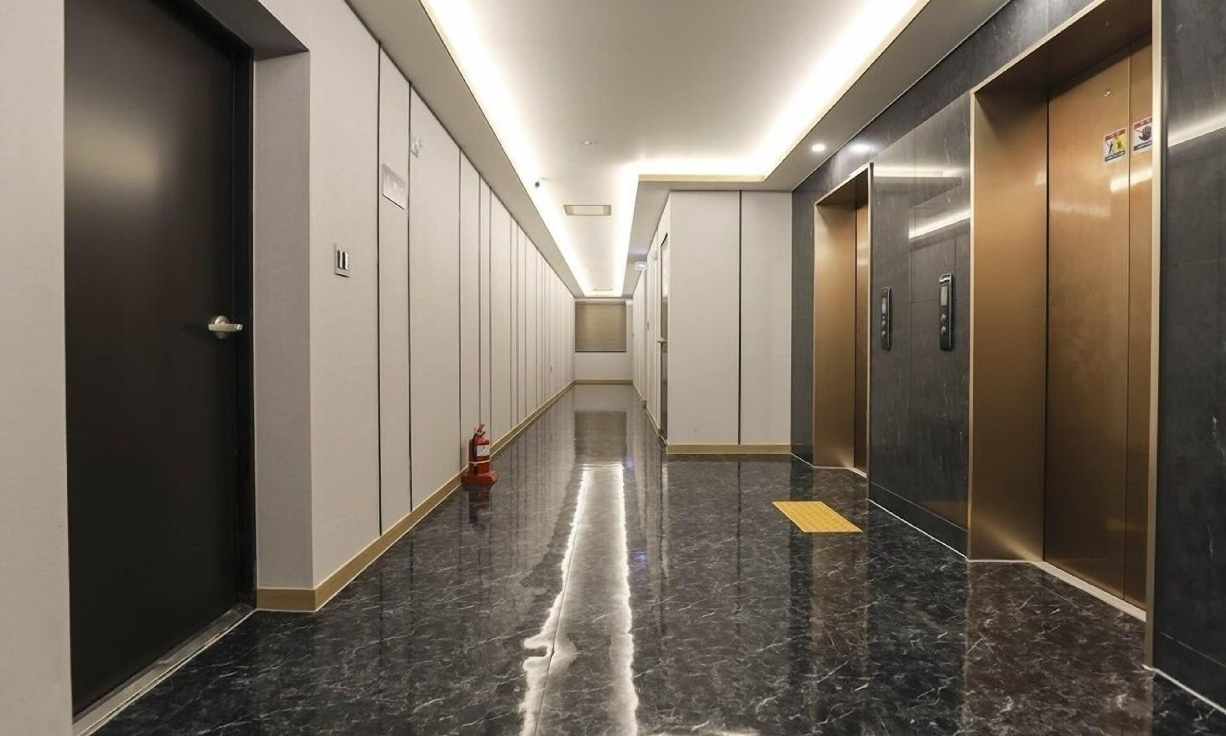 A modern hallway with a marble floor, a fire extinguisher, and two elevators.