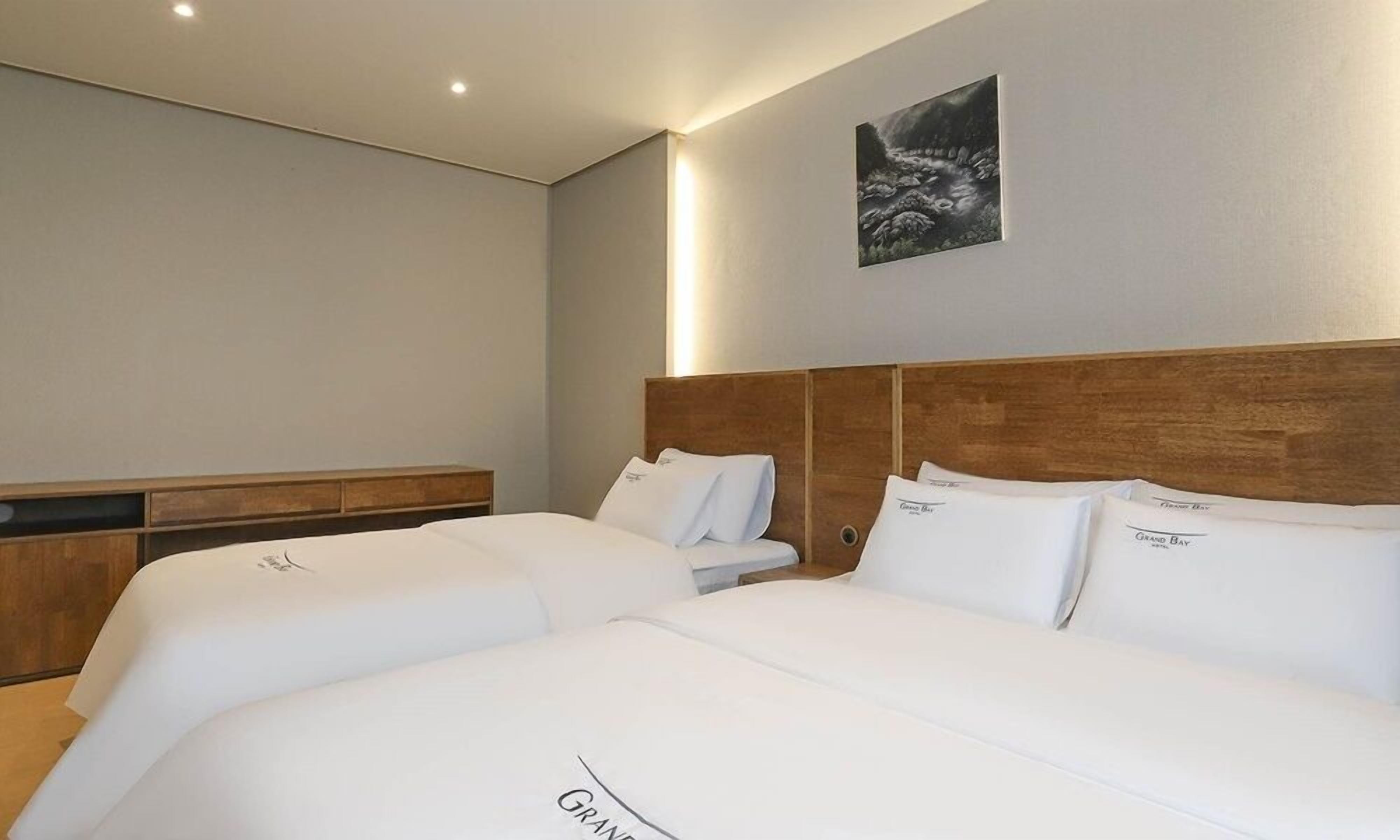 Habitación de hotel con dos camas, cabecero de madera, mesita de noche y un cuadro enmarcado en la pared.