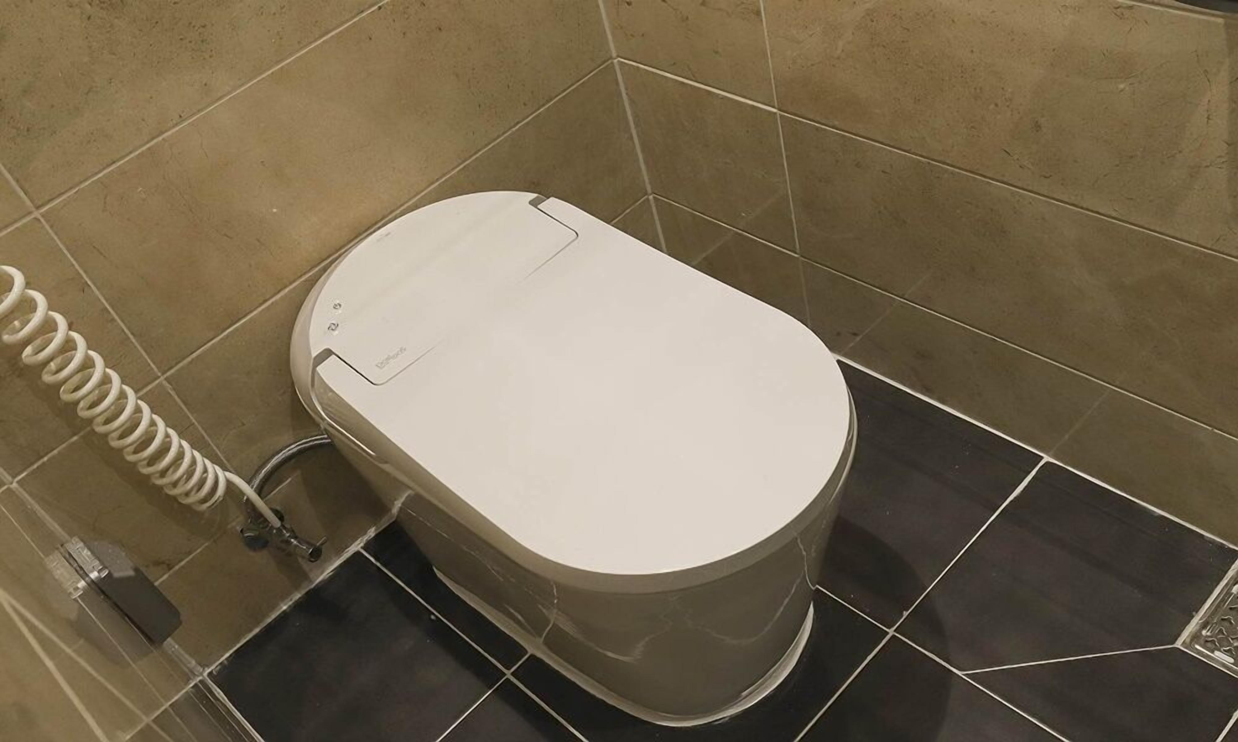 Un moderno WC con pedale, getto bidet e porta carta igienica.