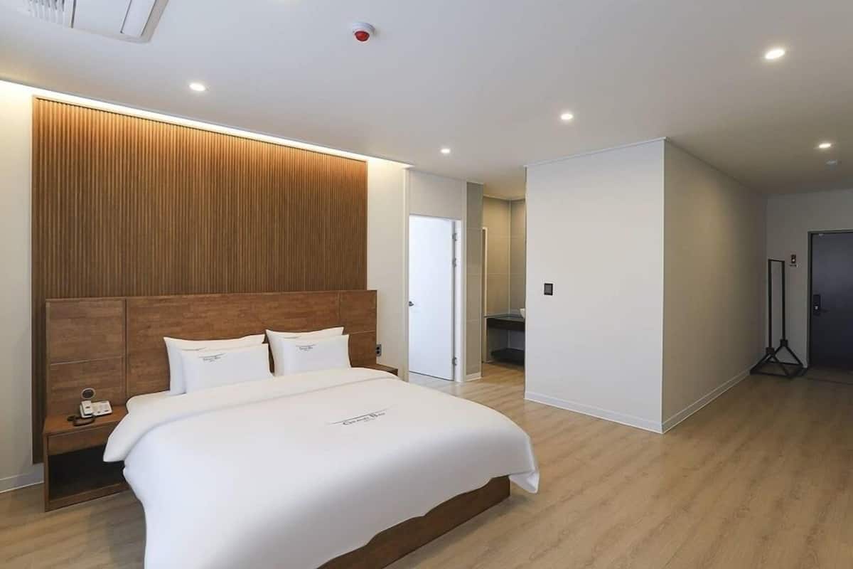 A modern hotel room with a large bed, wooden headboard, and a walk-in closet.