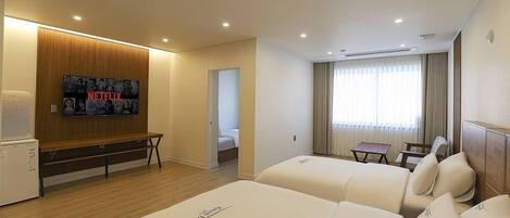 A hotel room with two beds, a TV mounted on the wall, a small table, and a window with curtains.