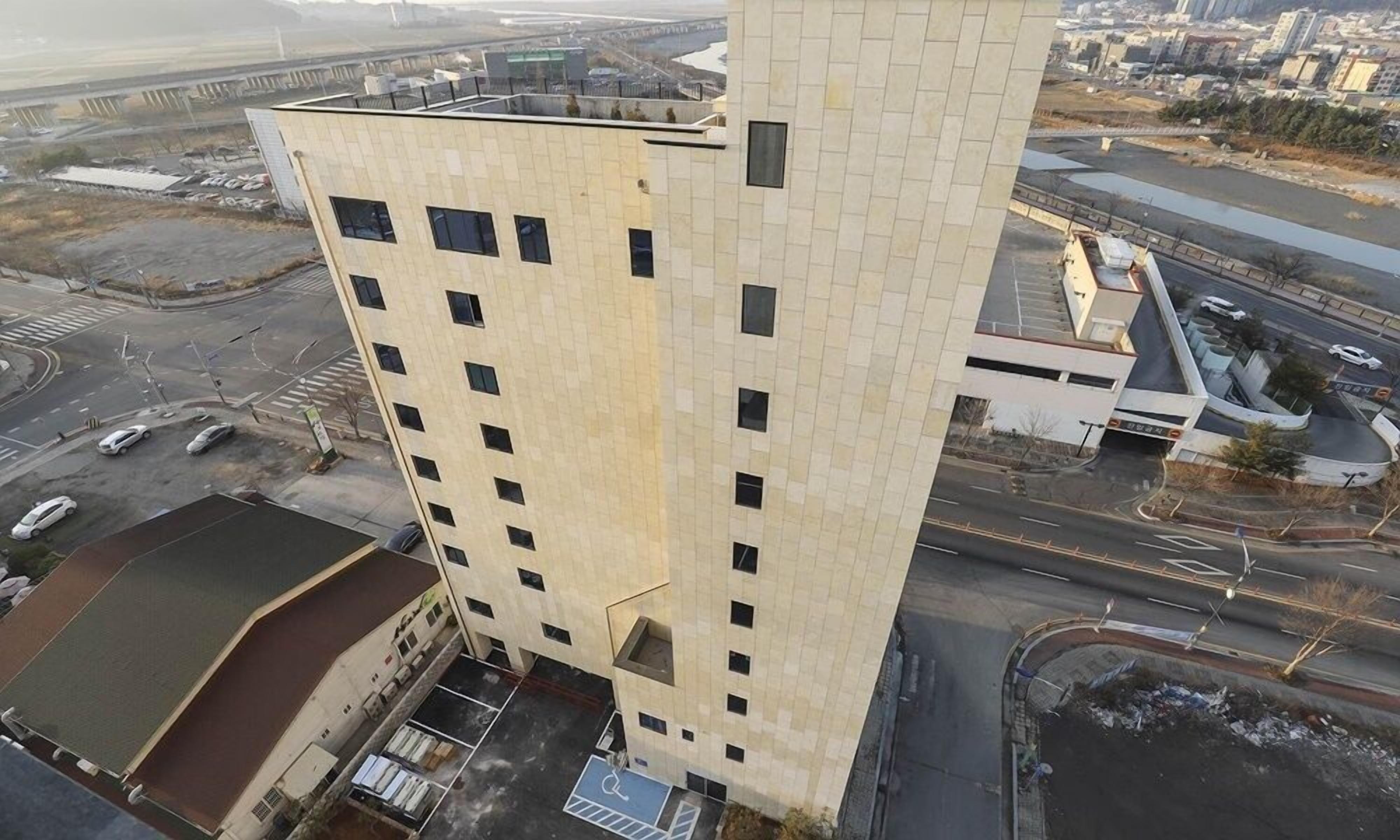 A high-rise building with multiple floors, a parking lot, and a bridge in the background.
