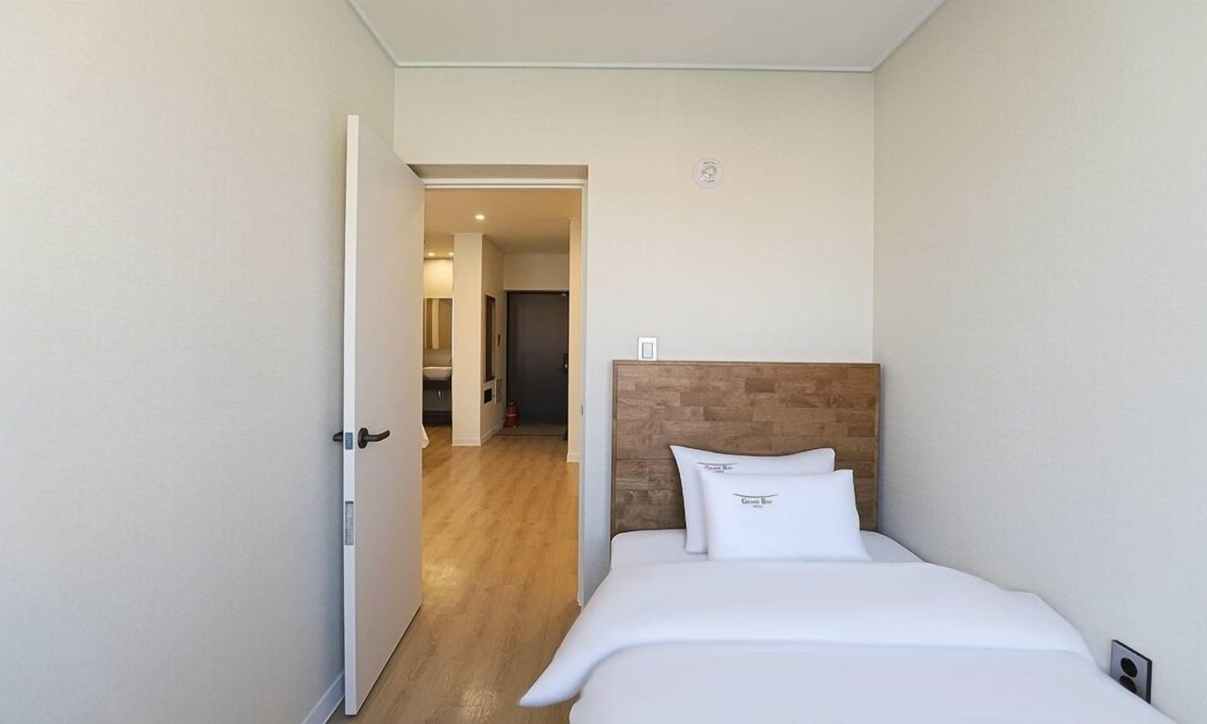 A hotel room with a wooden headboard, a bed with white bedding, and a door leading to a hallway.