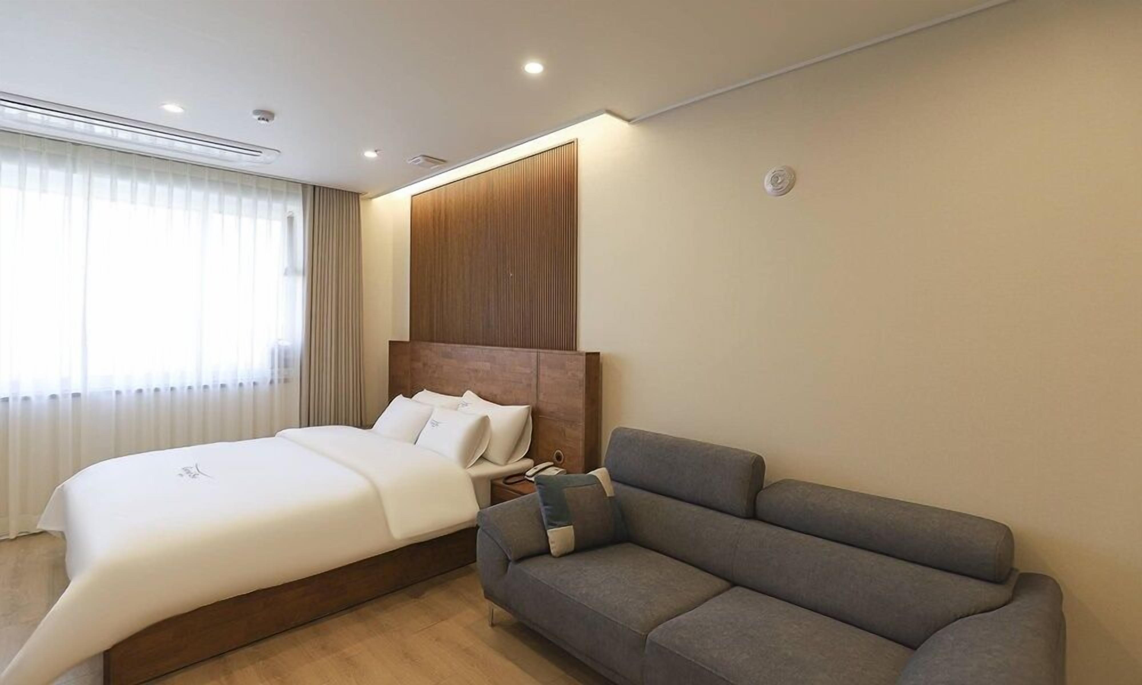 A modern hotel room with a large bed, a grey sofa, and a wooden headboard.
