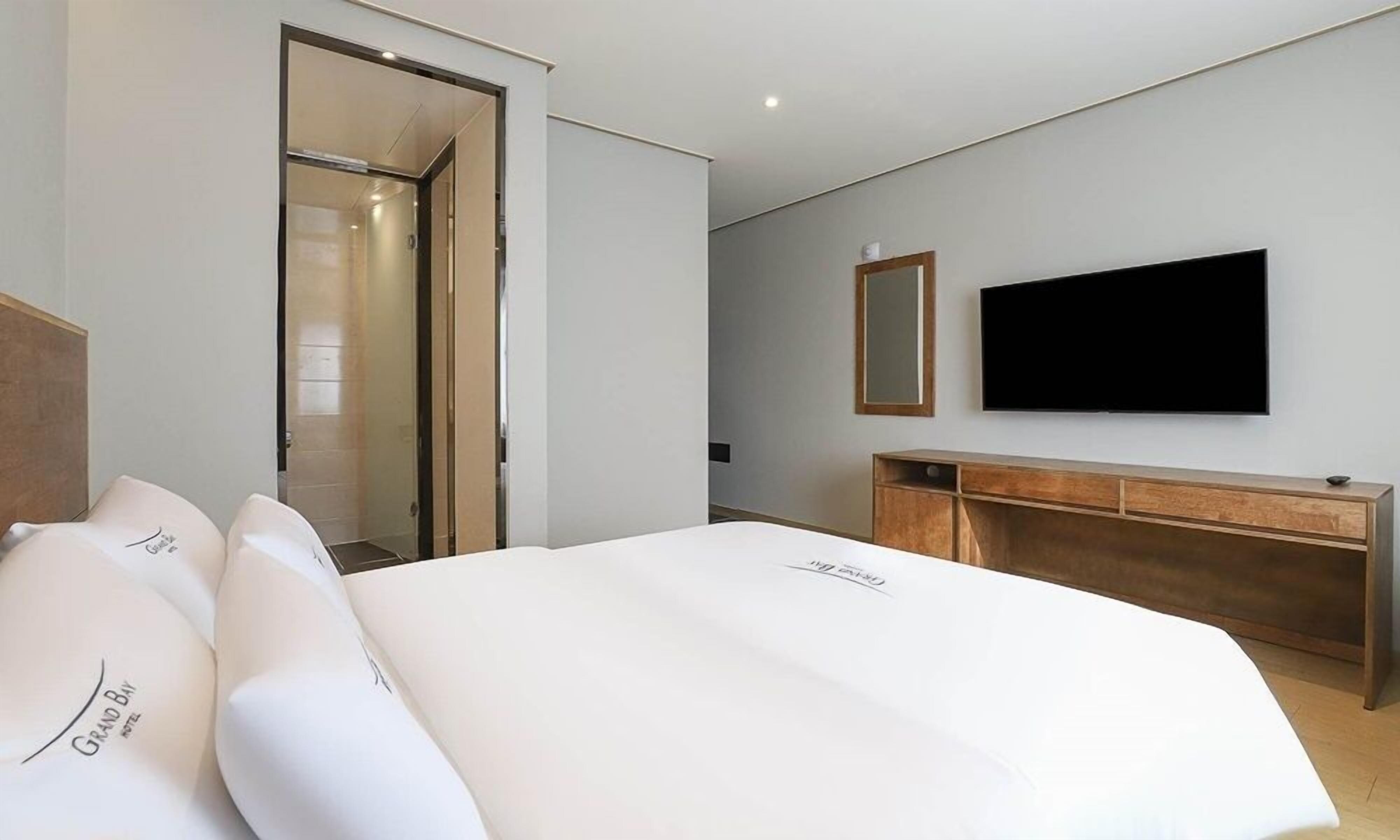 Ein Hotelzimmer mit einem Bett, einem an der Wand befestigten Fernseher, einer Holzkommode und einer Tür zu einem Badezimmer.