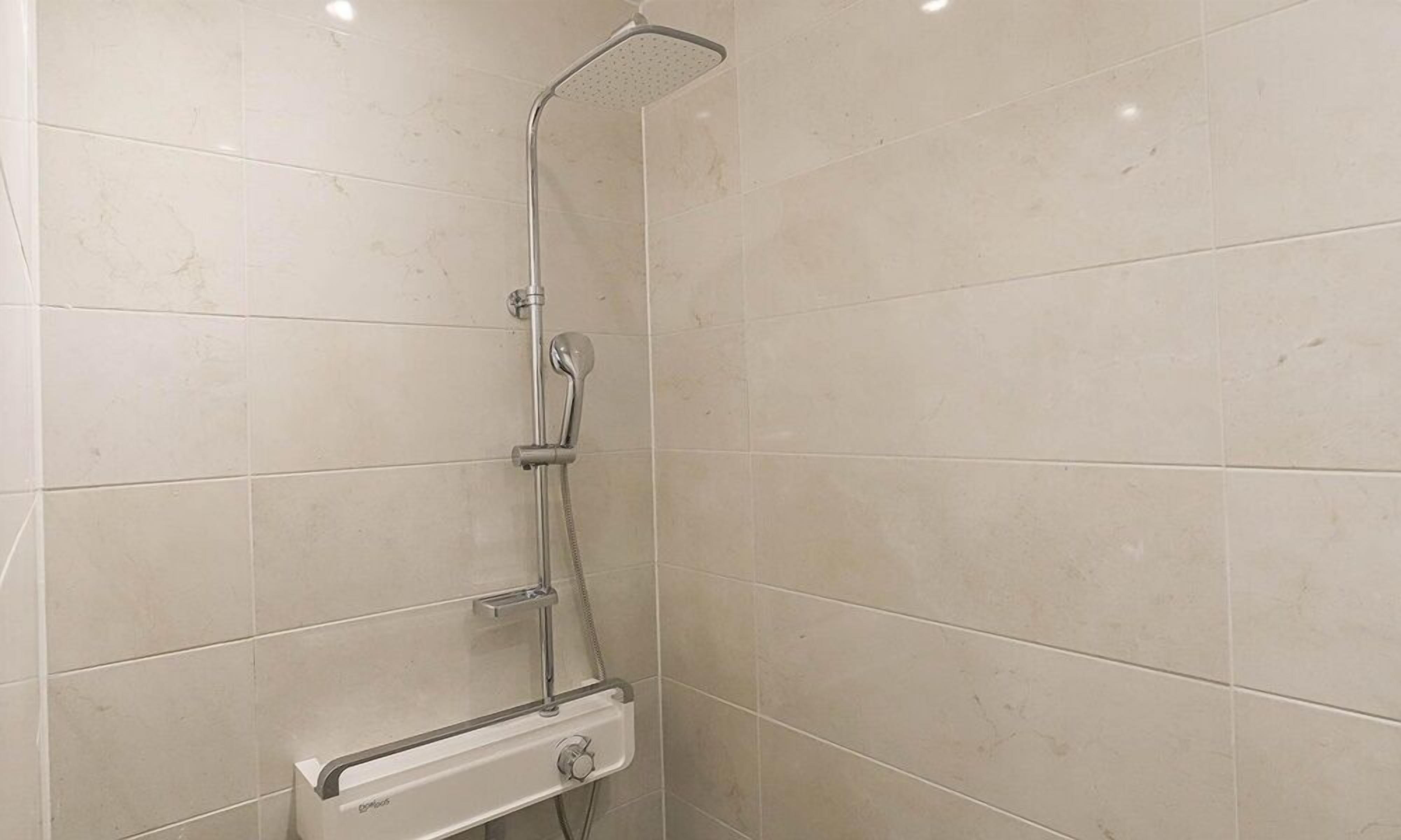 Un baño con ducha, paredes de azulejos y un panel de control.