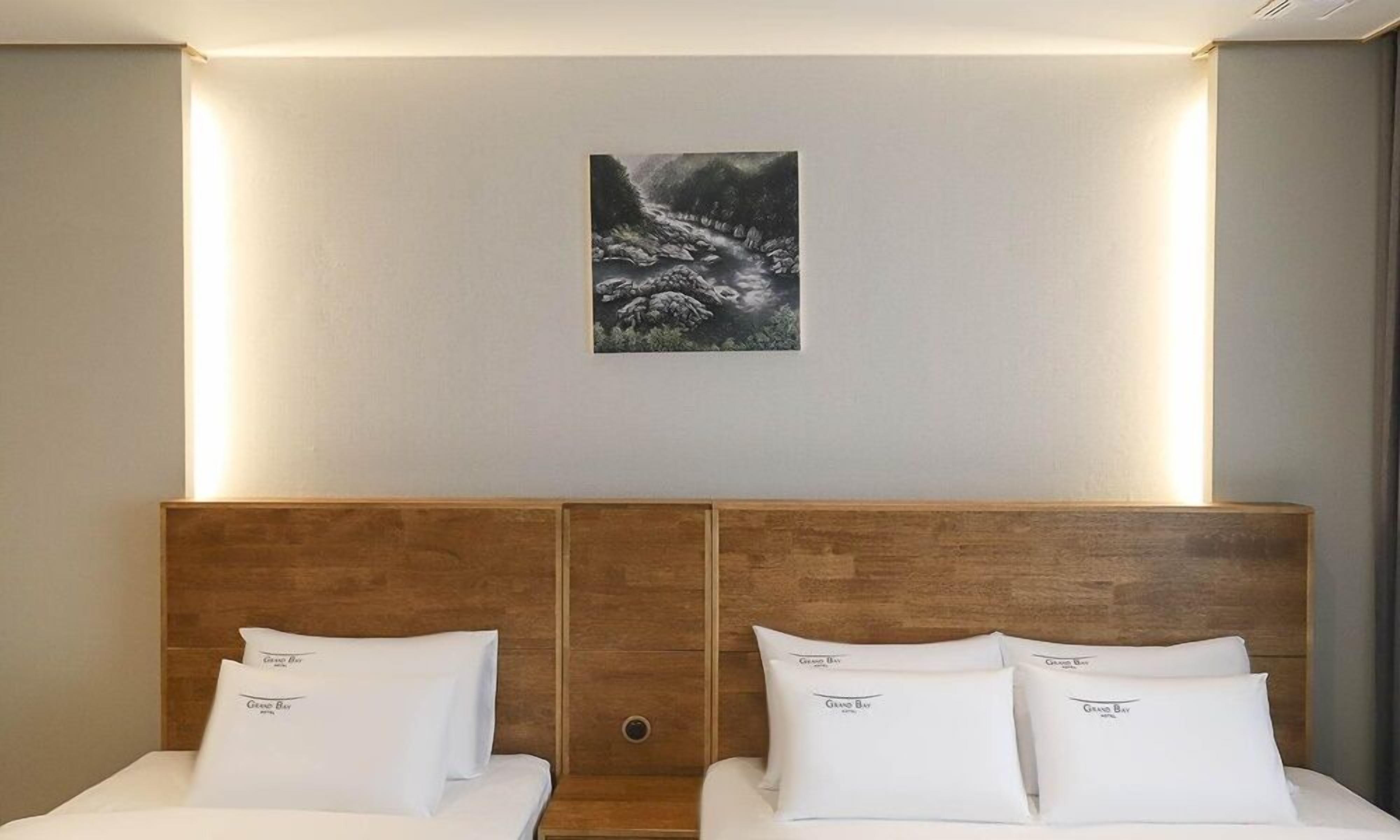 A hotel room with a wooden headboard, two beds with white bedding, and a framed artwork above the headboard.