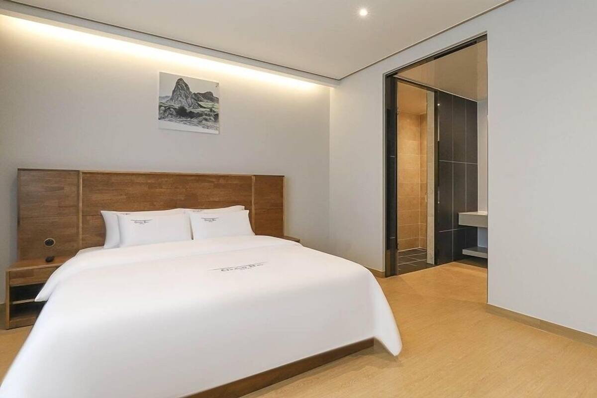 A modern hotel room with a large bed, wooden headboard, and a painting on the wall.