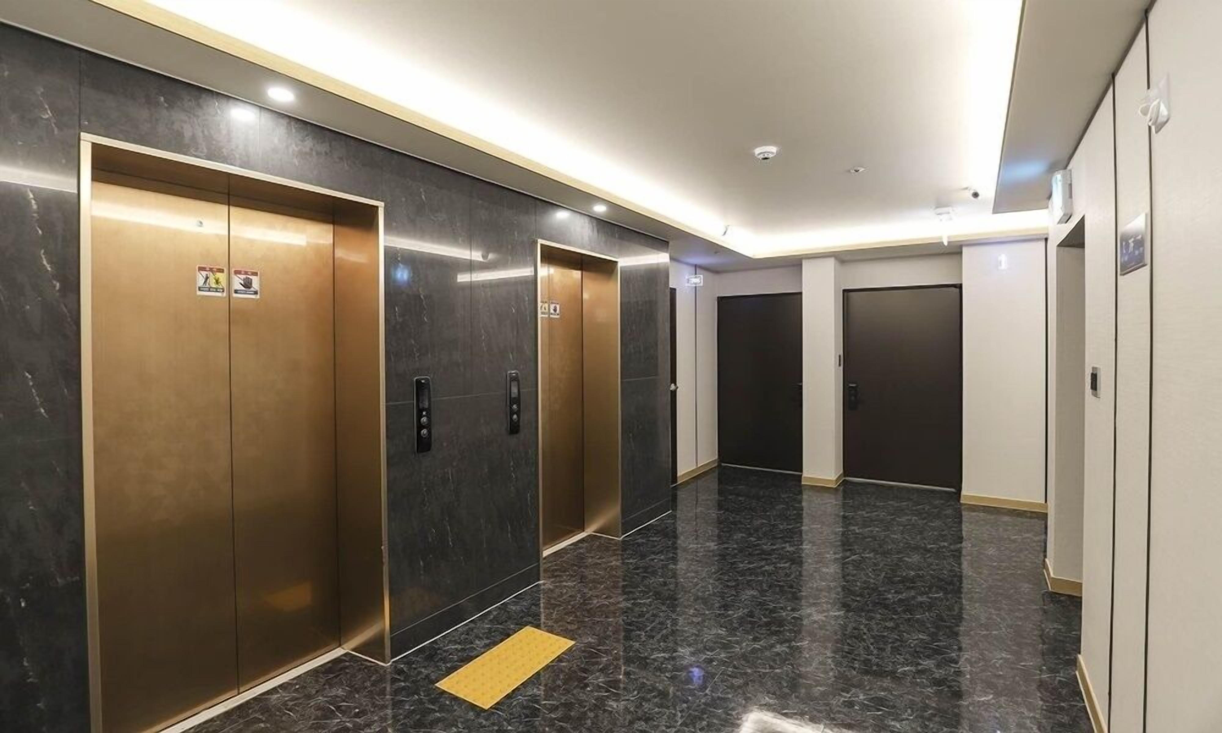 Un hall d’ascenseur moderne avec un sol en marbre et des portes d’ascenseur métalliques.