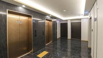 Un hall d’ascenseur moderne avec un sol en marbre et des portes d’ascenseur métalliques.