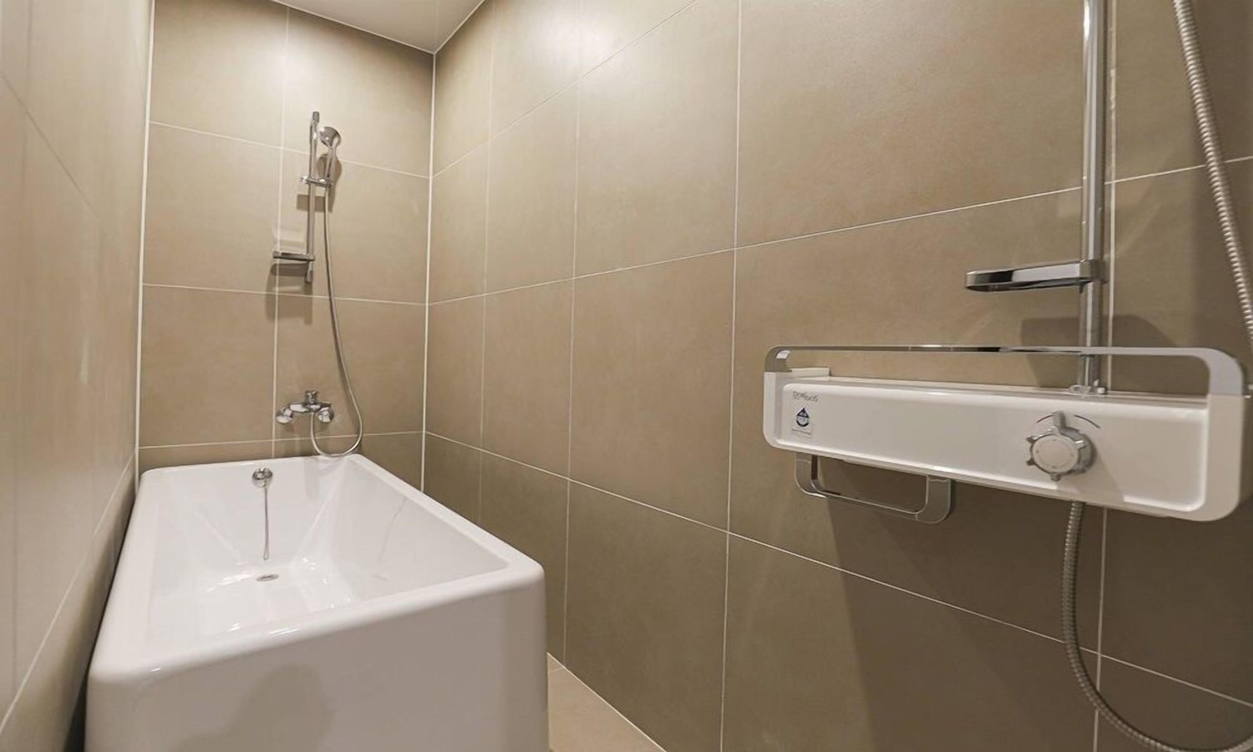 A bathroom with a white bathtub, a shower with a handheld showerhead, and a wall-mounted control panel.