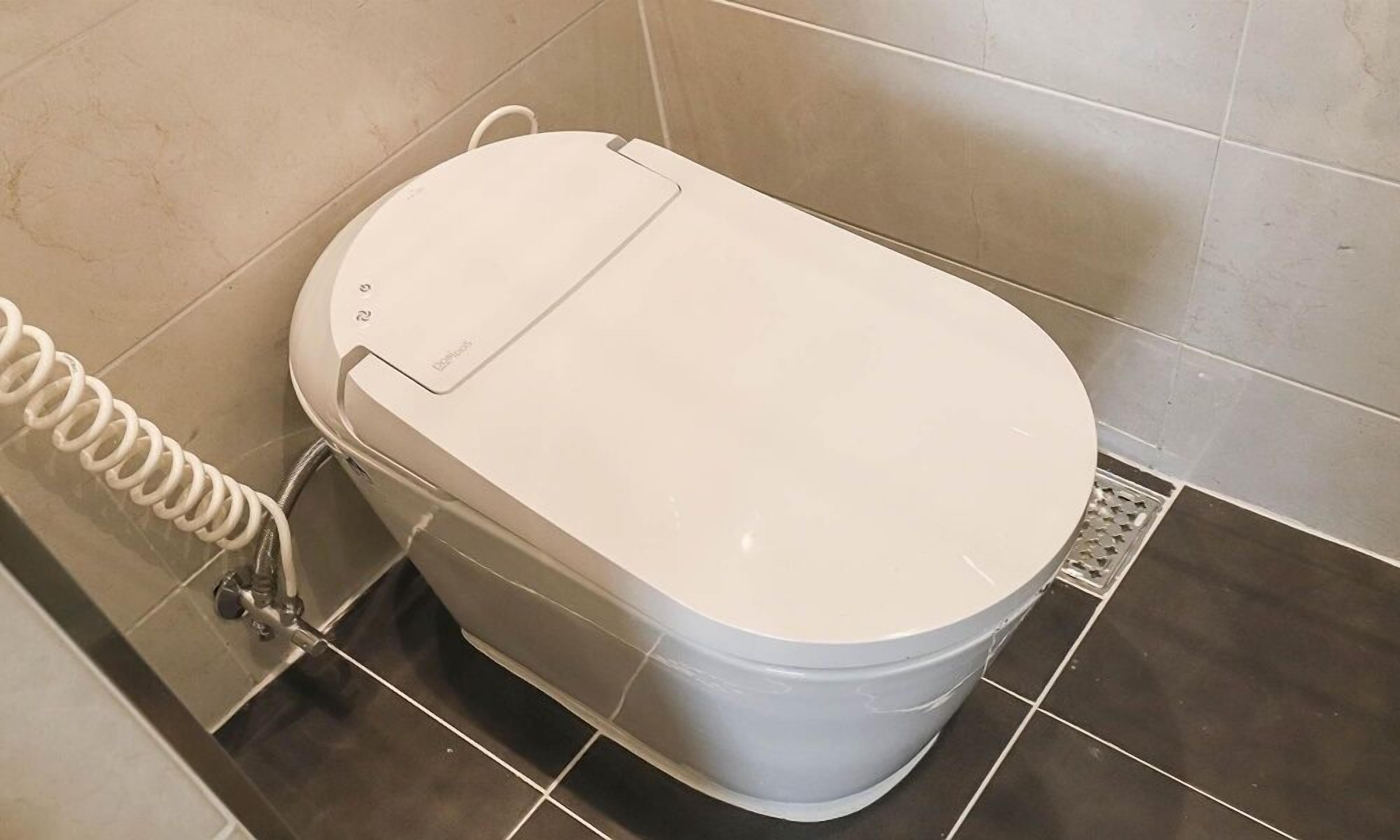 A white toilet with a lid and a coiled hose attached to the side.