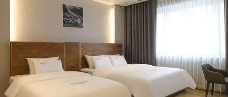 Ein Hotelzimmer mit zwei Betten, einem hölzernen Kopfteil, einem Bild an der Wand und einem großen Fenster mit Vorhängen.