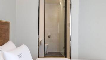 A hotel room with a bed, a wooden headboard, and a glass door leading to a bathroom with a toilet and a shower.