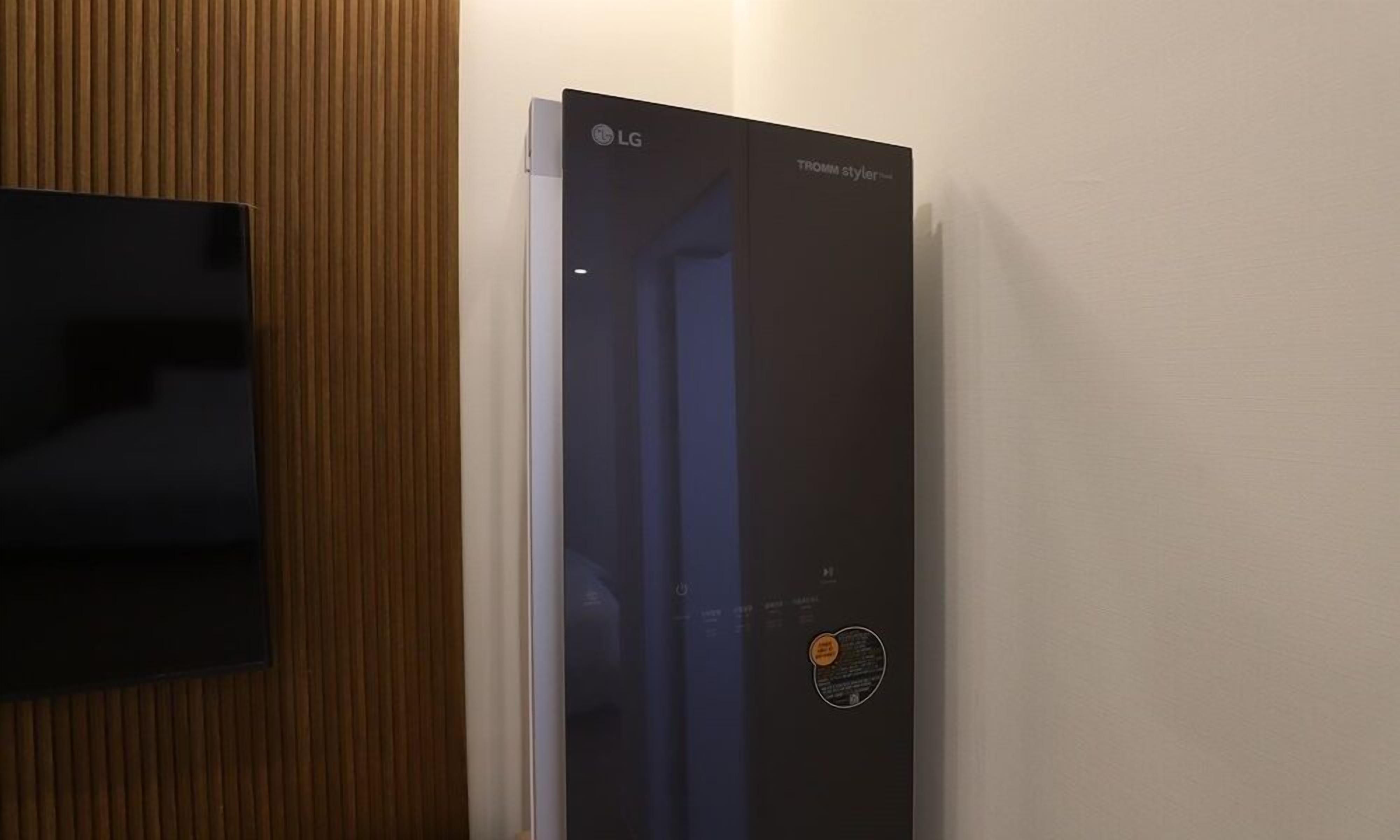 A modern room with a vertical wooden panel wall, a black LG refrigerator, and a flat-screen TV mounted on the wall.