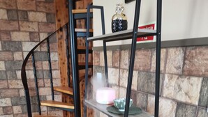 A staircase with a wooden finish, a metal railing, and a shelf unit against a brick wall.