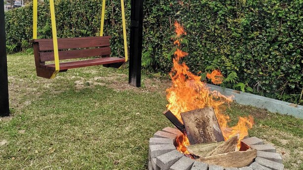 A fire pit with logs, a wooden swing, and a grassy area with a hedge and mountains in the background.