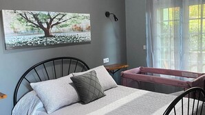 A bedroom with a bed, pillows, a nightstand, a window with curtains, and a wall-mounted lamp.