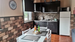 A kitchen with a brick wall, black cabinets, a white refrigerator, and a dining table with chairs.