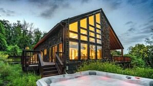 A wooden cabin with large windows, a hot tub, and a deck.