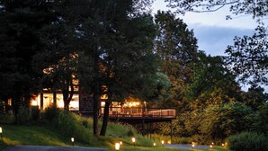 A pathway leading to a building with a wooden deck and a signboard, surrounded by trees and illuminated by ground lights.
