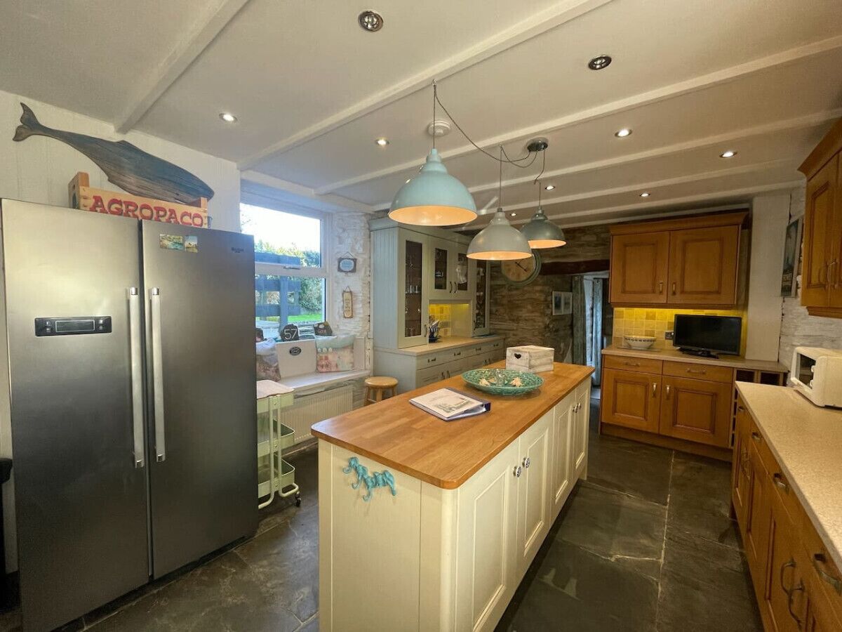 A kitchen with a central island, stainless steel refrigerator, wooden cabinets, and pendant lighting.