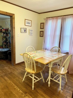 Un comedor con una mesa de madera y cuatro sillas, una estantería y cuadros en la pared.
