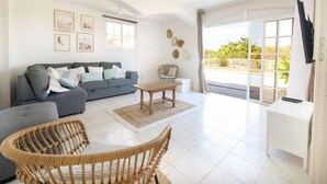 A spacious living room with a grey sofa, wicker chairs, a wooden coffee table, and a TV on a white stand. - Maison Oneway, Piscine Privée, Jardin Tropical. 8p (Sainte-Rose)