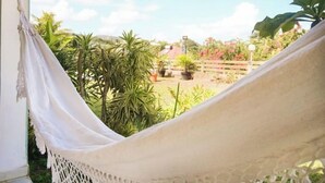 A hammock in a garden with various plants and a wooden fence in the background. - Maison Oneway, Piscine Privée, Jardin Tropical. 8p (Sainte-Rose)