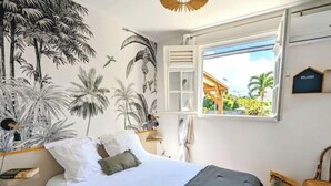 A bedroom with a bed, a window with a view, a wall mural, and a welcome sign. - Maison Oneway, Piscine Privée, Jardin Tropical. 8p (Sainte-Rose)