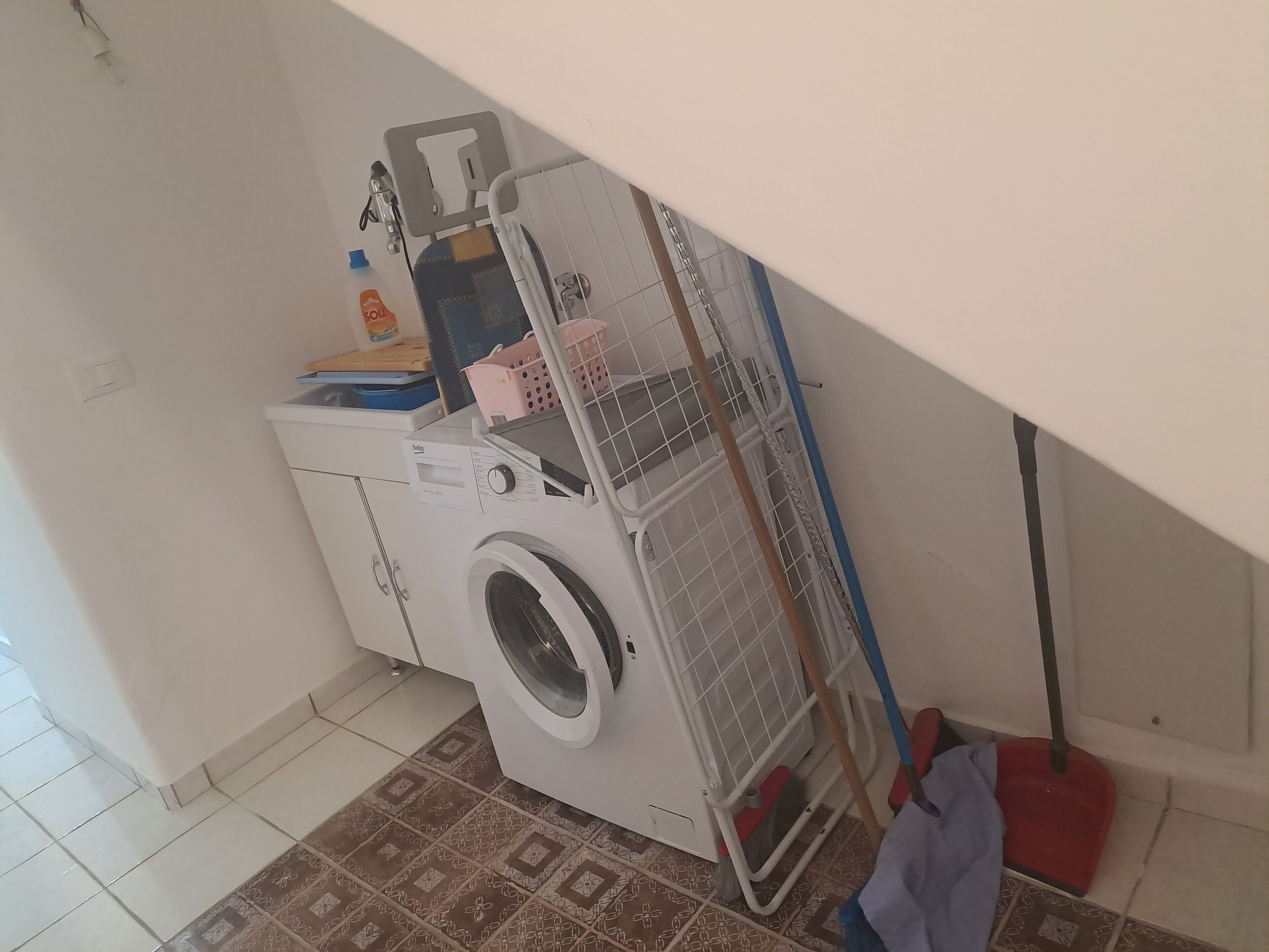 A laundry area with a washing machine, a drying rack, and a mop.