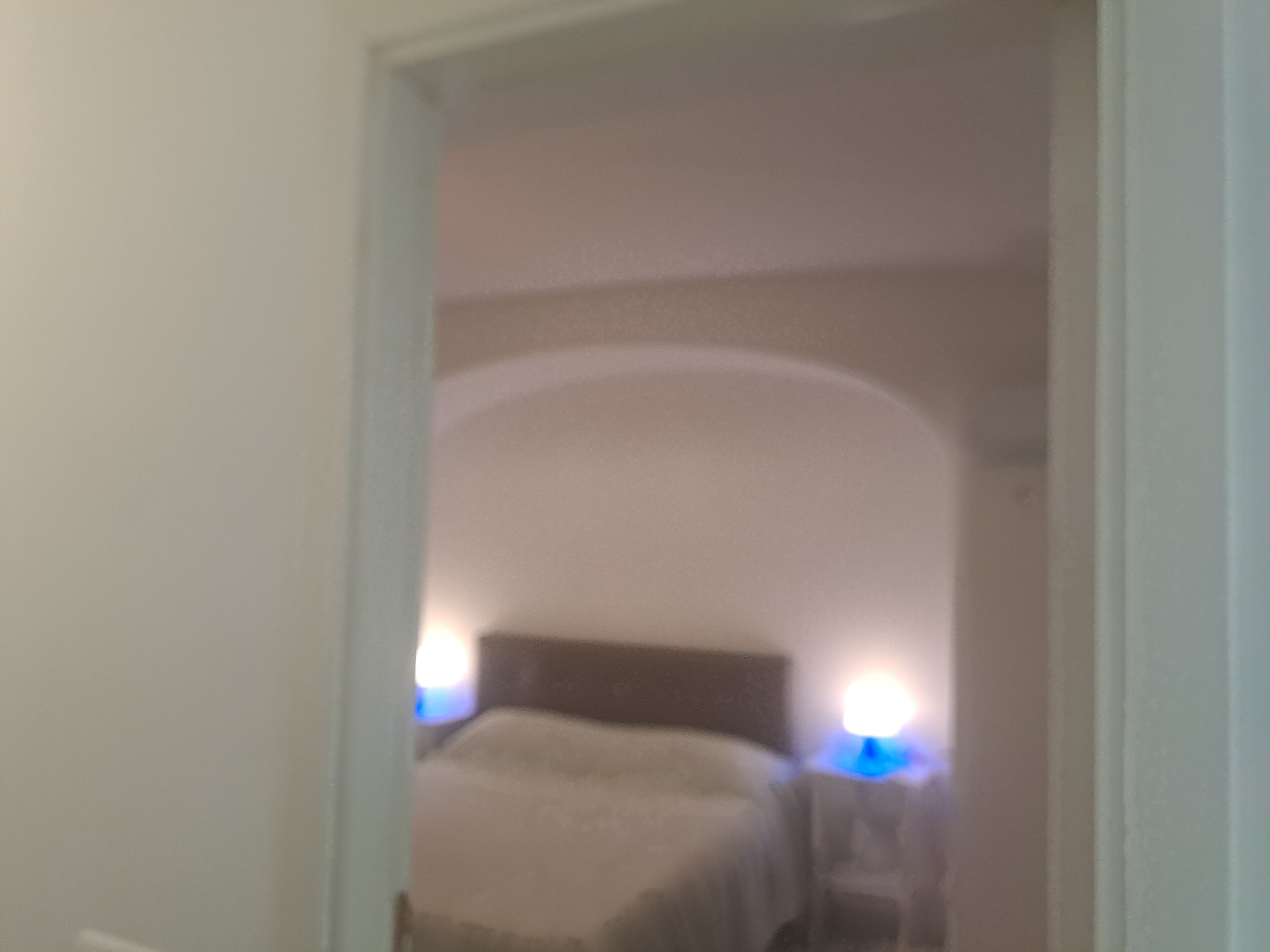 Un couloir étroit mène à une chambre à coucher équipée d’un lit et de lampes de chevet.