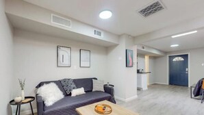 A modern living room with a dark-colored sofa, a wooden coffee table, and a small side table with a vase and a book. - ⟫Dog Run & Courtyard 2 Bedroom Apt w/King Bed W&D (Albuquerque)