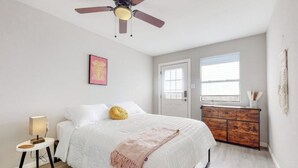 A bedroom with a bed, a ceiling fan, a bedside table with a lamp, a dresser, and a window with blinds. - ⟫Dog Run & Courtyard 2 Bedroom Apt w/King Bed W&D (Albuquerque)
