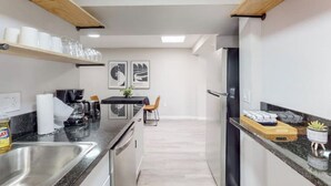 A modern kitchen with stainless steel appliances, wooden shelves, and a dining area with a table and chairs. - ⟫Dog Run & Courtyard 2 Bedroom Apt w/King Bed W&D (Albuquerque)